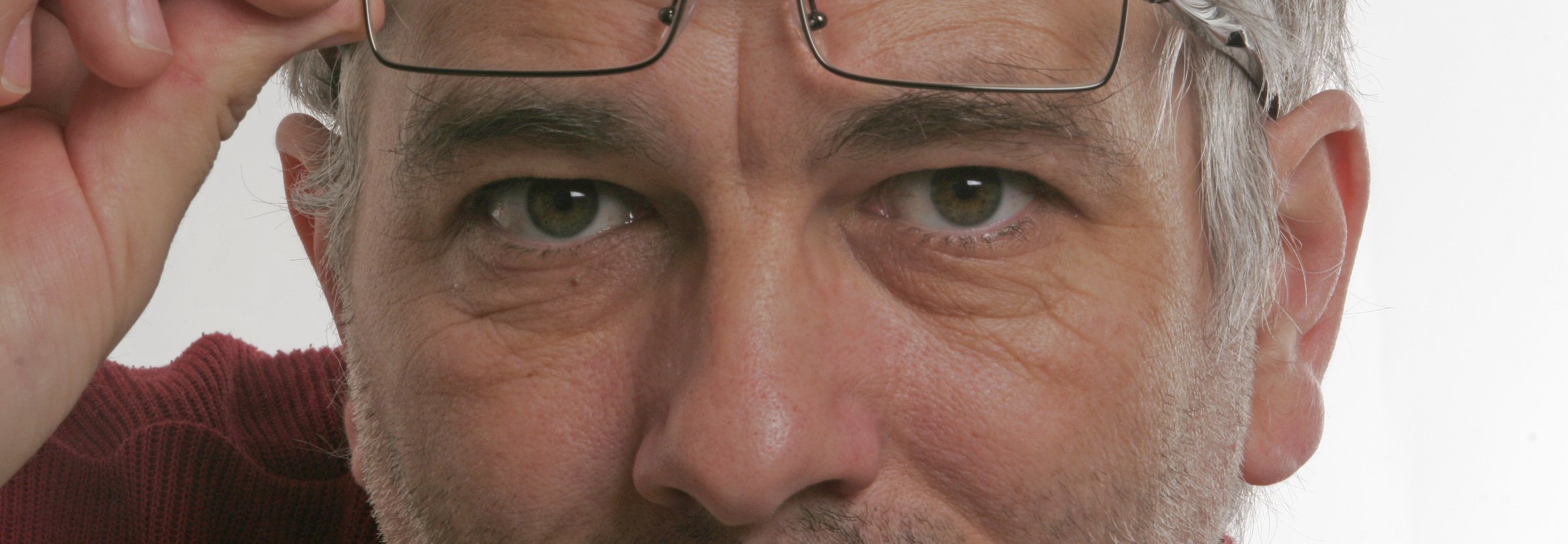 Mann ca. 60 Jahre hebt Brille um genauer zu sehen was vor sich geht. Führungstraining